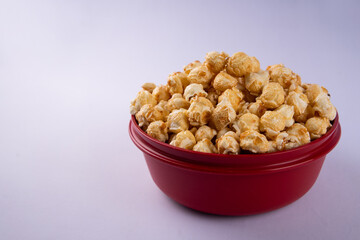 Close up of caramel popcorn in a red bowl, crunchy sweet snack with golden coating, isolated on light background