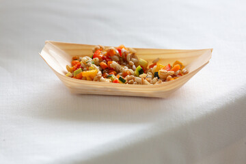 Wooden bowl presenting spelt with sautéed vegetables on white tablecloth