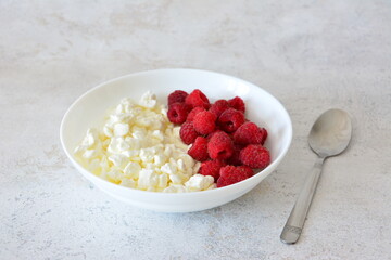 Cottage cheese with fresh raspberries in a white bowl close up
