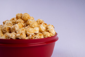 Close up of caramel popcorn in a red bowl, crunchy sweet snack with golden coating, isolated on light background
