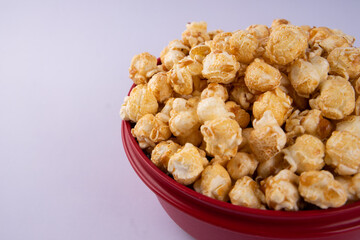 Close up of caramel popcorn in a red bowl, crunchy sweet snack with golden coating, isolated on light background