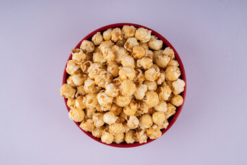 Flat lay view of caramel popcorn in a red bowl, crunchy sweet snack with golden coating, isolated on light background