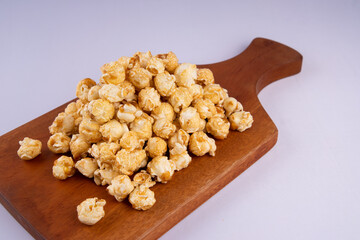Pile of caramel popcorn on wooden cutting board, crunchy golden sweet snack isolated on light background, perfect for food photography and snack concept