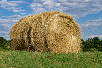 A golden hay bale sits in a lush green field with a vibrant blue sky filled with clouds.