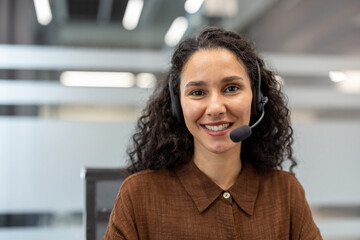 Customer service operator with headset smiles confidently at camera in modern office, offering...