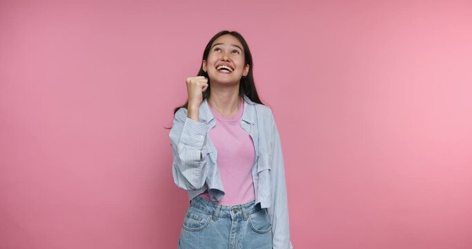 Smiling girl celebrates success with joy and excitement in a pink studio setting