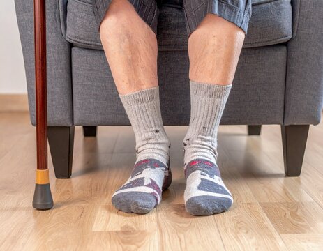 An image showing the feet of an old man, accompanied by a walking stick.