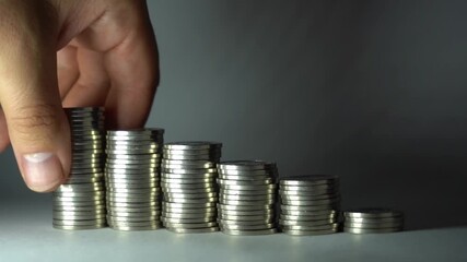 Hand removes coins from a tall stack and places them below, showing fund redistribution, spending control, cash-flow adjustment, and practical money management.