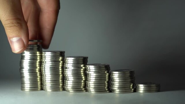 Hand removes coins from a tall stack and places them below, showing fund redistribution, spending control, cash-flow adjustment, and practical money management.