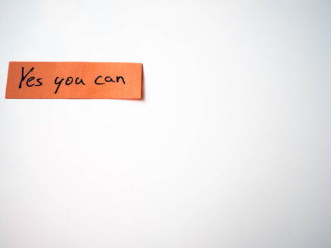 The phrase "Yes you can" handwritten on an orange sticky note against a white background