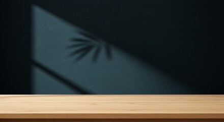A moody wooden table with a shadowy plant on a wall.