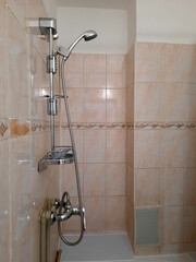 A chrome shower head with a flexible hose and soap and shampoo dispenser on a tiled bathroom wall.
