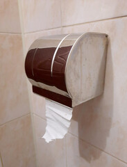A metal toilet paper holder with a roll on a tiled bathroom wall, side view.
