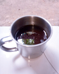 A black coffee, served in a stainless steel cup and brought to you from above.