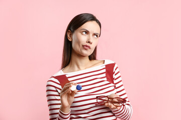 Woman choosing between glasses and contact lenses on pink background