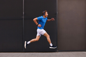 Obraz premium Man in headphones running near building on city street