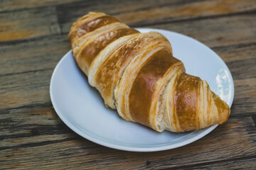 French croissant on wooden tabletop. Fresh croissant on wooden table. Golden baked croissant on wooden background.
