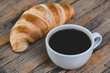Fresh croissant and hot coffee. Cup of coffee and croissant. Breakfast with coffee and croissant. Cup of coffee with croissant on table.