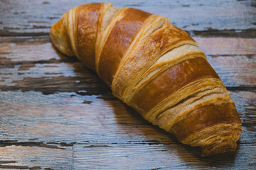 French croissant on wooden tabletop. Fresh croissant on wooden table. Golden baked croissant on wooden background.