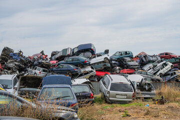 Stacked wrecked cars in a chaotic junkyard under a clear sky, symbolizing automotive waste and...