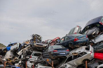 Stacked wrecked cars in a chaotic junkyard under a clear sky, symbolizing automotive waste and recycling.
