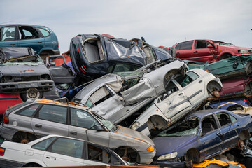 Stacked wrecked cars in a chaotic junkyard under a clear sky, symbolizing automotive waste and...