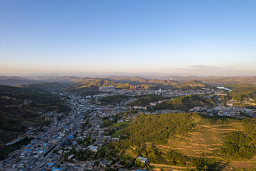 A wide view shows buildings nestled among green hills under a clear sky.