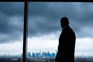 Businessman silhouette at office window overlooking stormy skyline, concept of uncertainty,