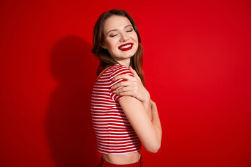 Smiling woman posing on a vibrant red background wearing striped shirt and showcasing happiness and...