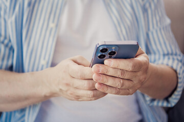 Mature individual using a smartphone indoors, demonstrating mobile technology, casual lifestyle, and modern connectivity
