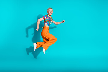 Joyful woman jumps energetically on a turquoise background wearing a vibrant outfit and expressing happiness