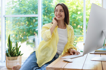 Woman using computer at wooden desk indoors. Home workplace