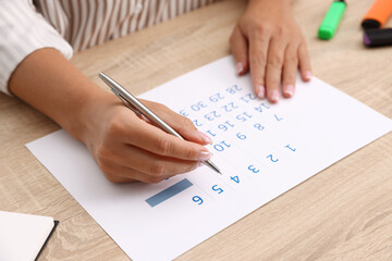 Business planning. Woman using calendar at wooden table in office, closeup