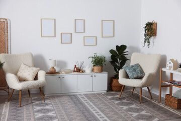 Stylish armchairs with cushions, cabinet, houseplants and decor in room. Interior design