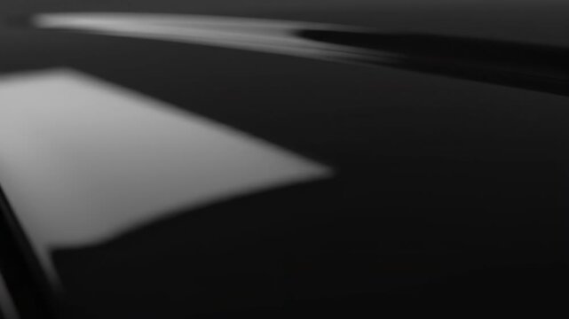 Shiny Black Plastic Texture - Close-up shot of a sleek, black plastic surface with subtle reflections and shadows. The horizontal format emphasizes the material's smooth, shiny texture.
