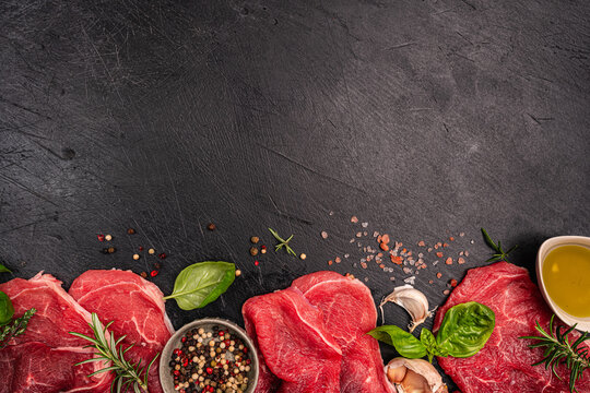 Raw organic steak with ingredients for cooking on a dark slate, stone or concrete background. Top view with copy space. High quality photo - Powered by Adobe