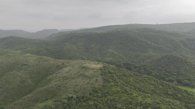 Aerial drone video of lush green Aravalli mountains near Rajsamand and Udaipur in Rajasthan, India, filmed after the monsoon season with dramatic cloudy skies enhancing the scenic landscape view.