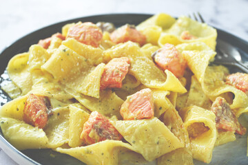 papardelle pasta, in creamy sauce with salmon, homemade, on a gray background, no people,