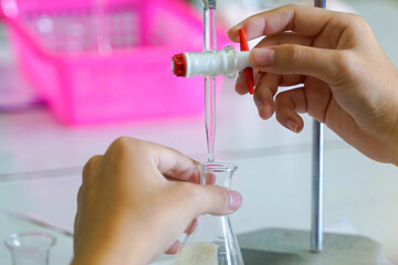 Close-up of hands meticulously operating a burette, dripping liquid into a lab flask. Emphasizes...