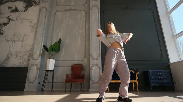 Stylish talented young woman dancing contemporary hip-hop in a spacious, sunny studio, performing an energetic and expressive choreography with modern street dance moves and passion
