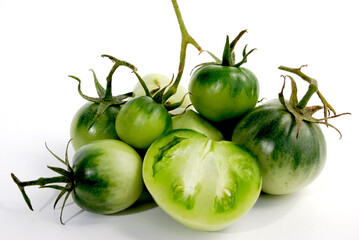 small green whole tomatoes of various sizes with a tomato cut in half on a white background