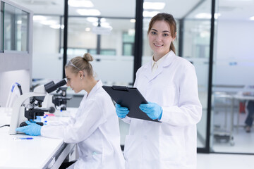 Femail scientist wearing a lab coat holding a tablet and smiling in a modern laboratory