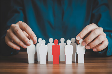 Hands arrange wooden figures with one red figure standing out representing leadership and individuality