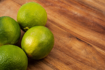 Four fresh limes sit neatly on a wooden cutting board, showcasing their vibrant green color and textured skin, illuminated by natural light from a nearby window.