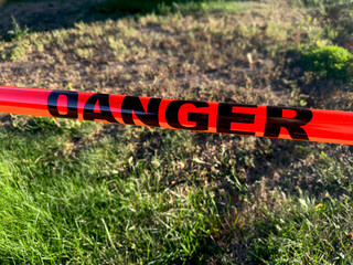 Close-up of bright red danger tape stretched across a grassy outdoor area, serving as a warning and safety precaution in a restricted or hazardous zone