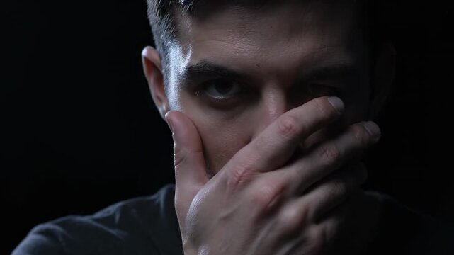Intense Man Partially Hiding Face - Close-up shot of a man's face, partially obscured by his hand, conveying a sense of intensity or secrecy.