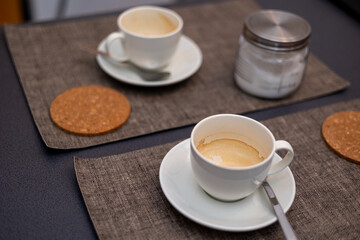 Used white coffee cups with coffee residue and cork coasters on wooden table in cafe setting