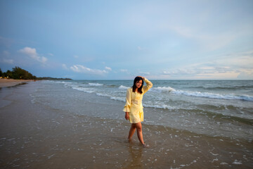 Beautiful Asian woman is happily strolling along the beach as the waves crash against her back. Happy girl rejoices in summer vacation.