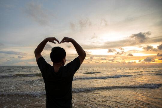 The silhouette of a man who raised his hand to create a heart shape in the sea at sunset