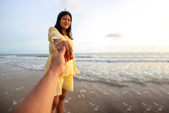 Couple having fun on the beach. A happy young woman is holding hands with a man. beautiful young woman in a bright yellow dress is walking along the beach